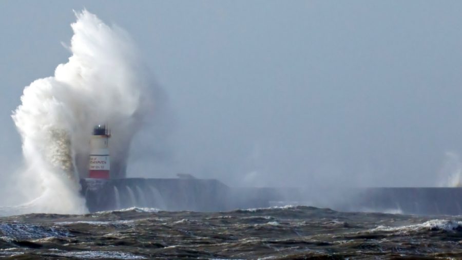 Newhaven Lighthouse in East Sussex in windy weather with waves breaking over lighthouse light barely visible.