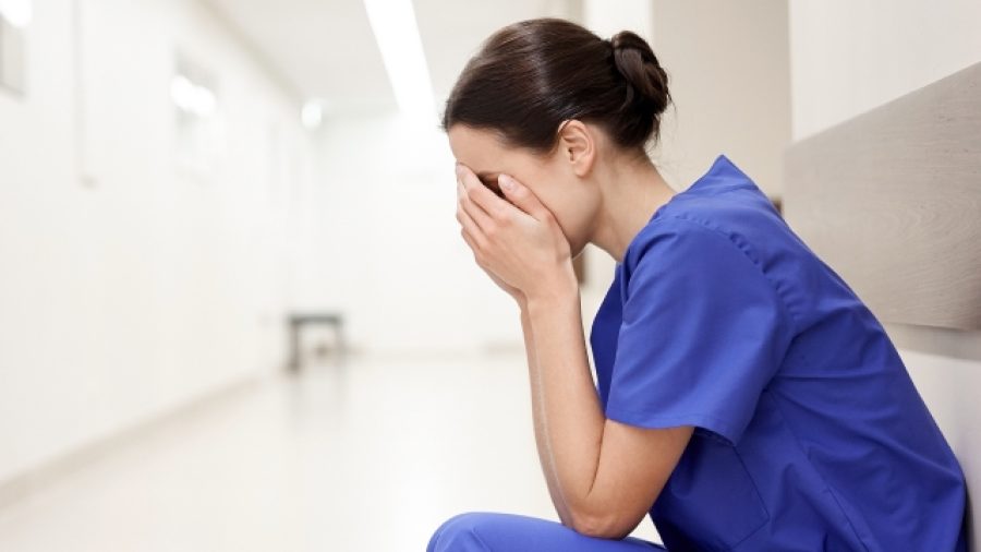 people, medicine, healthcare and sorrow concept - sad or crying female nurse at hospital corridor