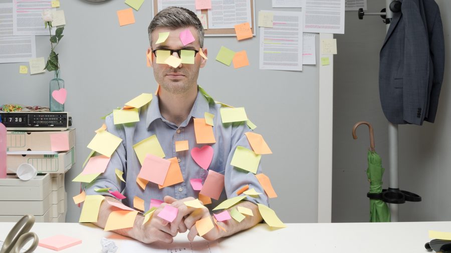 Office worker sitting at desk covered with colorful post it stick notes.